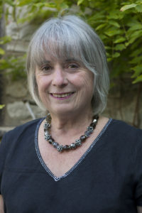 Woman with chin length greay hair smiling. Sparkly necklace.